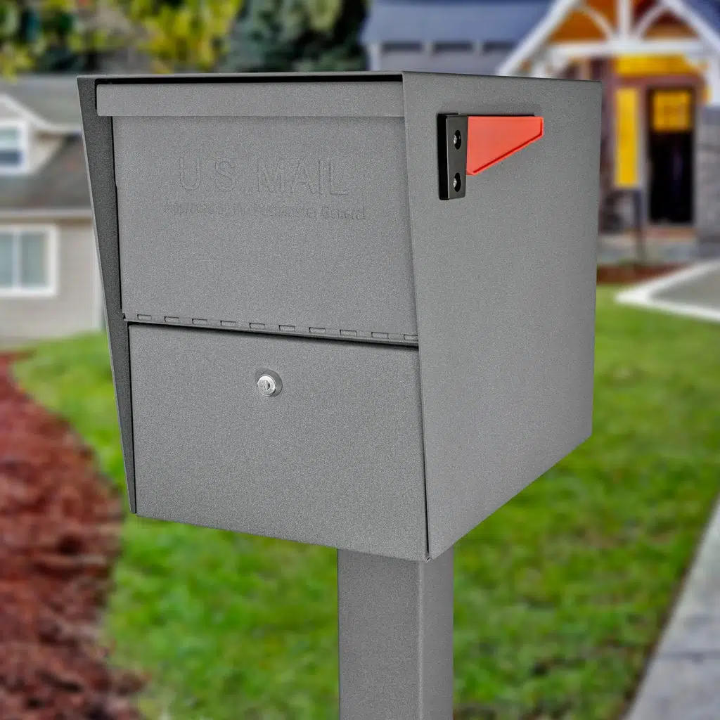 A gray mailbox with a red flag on a post outside a house.